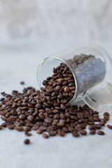 Roasted coffee beans spilling from clear glass mug on its side onto stone cement textured surface