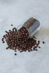 Roasted coffee beans spilling from clear glass mug on its side onto stone cement textured surface