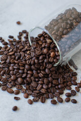 Roasted coffee beans spilling from clear glass mug on its side onto stone cement textured surface