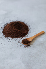 A heap or pile of dark brown ground coffee on a neutral blurred textured background with coffee on a wooden spoon