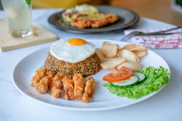 Fried rice with fried egg and fried chicken slices coated in flour, then topped with sliced ​​tomatoes, cucumber and celery leaves.