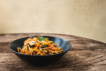 Homemade Spicy Sausage Spaghetti with basil on the black plate on the wooden table, Thai style