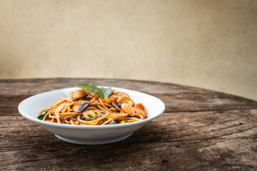 Homemade Spicy Sausage Spaghetti with basil on the white plate on the wooden table, Thai style