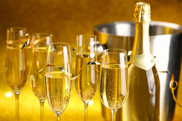 Champagne in glasses, bottle and ice bucket on golden background, closeup