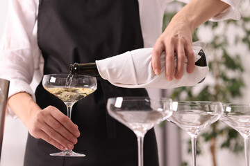 Waiter filling glasses with champagne indoors, closeup