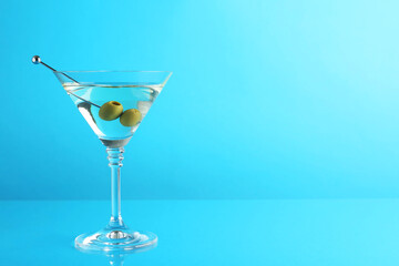 Martini cocktail with olives in glass on light blue background, space for text