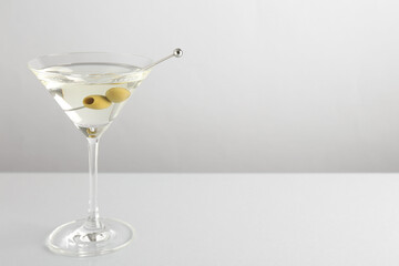 Martini cocktail with olives in glass on light table, space for text