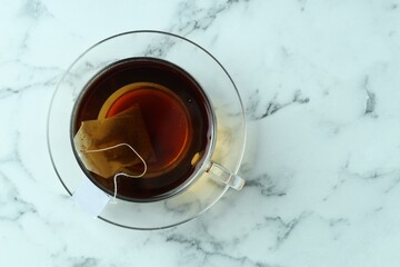 Tea bag in glass cup with hot drink on light marble table, top view. Space for text