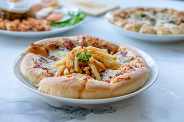 Pizza with fries on a white marble table with other dishes