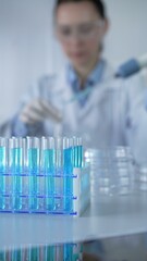 Test tubes with a blue liquid, close-up view. Scientist holding pipette conducting experiments in...