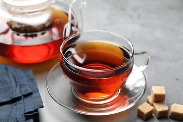 Aromatic black tea and brown sugar cubes on light grey table, closeup