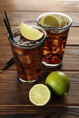 Refreshing iced cola with lemon slices and lime on wooden table, closeup