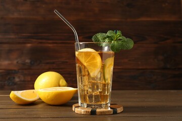 Refreshing iced tea with slices of lemon, lime, mint and drinking straw on wooden table