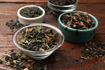 Different dry tea leaves in bowl on wooden table, closeup
