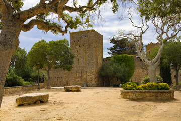 Torre de vigilancia y muralla medieval rodeadas de árboles y jardines en Pals, Cataluña, España.