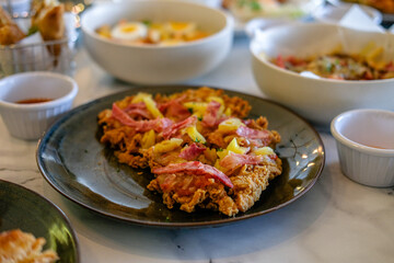 Fried chicken with shredded beef and macaroni pasta served on a black plate with other dishes