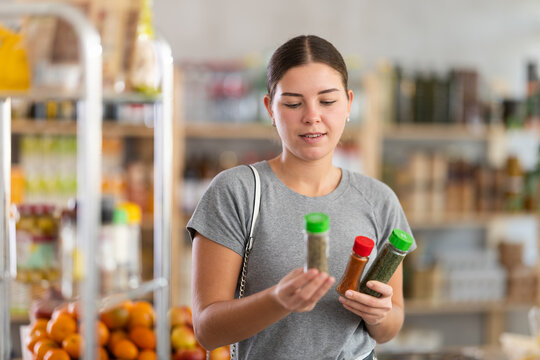 Joyful woman holds jars of spices and seasonings in her hands in a supermarket. European woman chooses natural seasonings for cooking meat and fish for dinner - Powered by Adobe