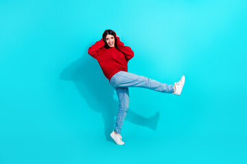 Stylish brunette woman in red sweater and jeans showing a joyful expression against a turquoise background