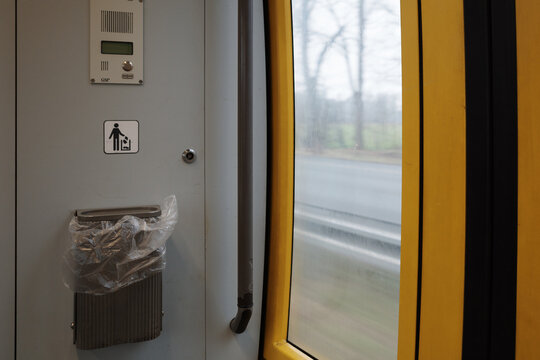 A close-up view inside a public transport vehicle, possibly a train or tram, featuring a mounted trash bin with a plastic liner, a waste disposal sign, and an intercom panel. 