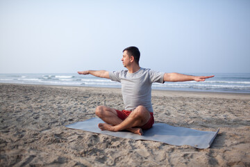 The man does yoga on  the sea beach to meditate. The man is wearing sports clothes, a shorts and...