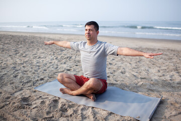 The man does yoga on  the sea beach to meditate. The man is wearing sports clothes, a shorts and...