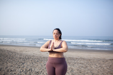 plus size girl does yoga on  the sea beach to lose weight and keep fit. The woman is wearing sports...