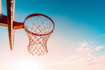 A classic basketball hoop standing against a gradient sunset sky, with its net gently swaying