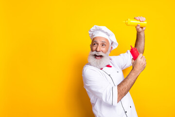 Naklejka premium Senior Chef Enthusiastically Holding Mustard and Ketchup Bottles in Vibrant Yellow Background Setting