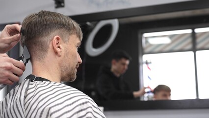 Professional barber trimming male client's hair using electric razor, creating precise haircut in barbershop setting with sleek styling tools