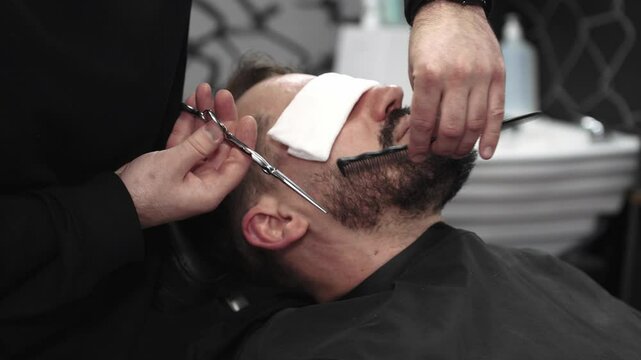 Professional barber carefully trimming beard with scissors, creating clean lines and sharp detailing inside contemporary barbershop workspace