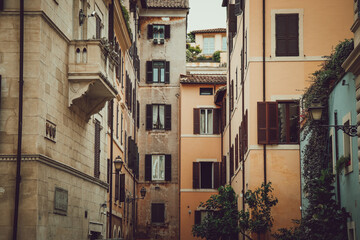 A narrow street lined with tall, closely packed buildings in warm tones. The buildings have...