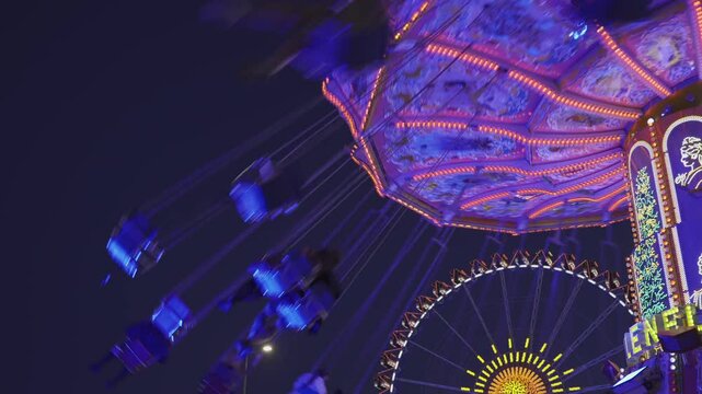  Munich, Germany. Viennese carousel at amusement park during Oktoberfest in evening with beautiful lighting. Wellenflug auf Wiesen Thereianwiese in Munchen. Wellenflieger Oktoberfest. 