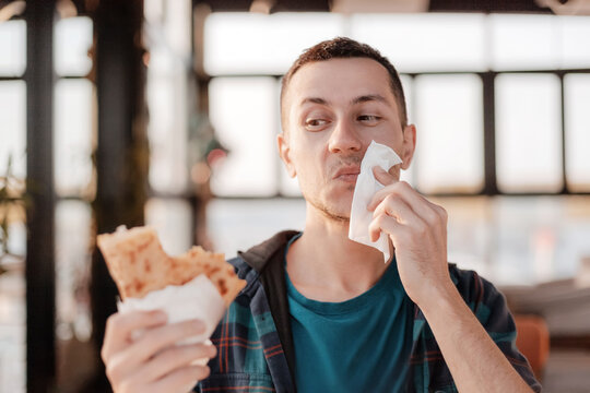 Fototapeta Young man cleaning his face with a white napkin while enjoying a delicious piadina in a cozy restaurant setting