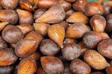 A close-up display of a large quantity of salak (snake fruit), highlighting their scaly brown skin texture and natural shine