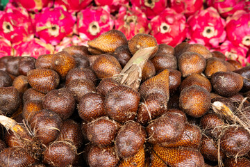 A display of salak (snake fruit) and dragon fruit, highlighting their contrasting textures and vibrant colors in a market or store setting