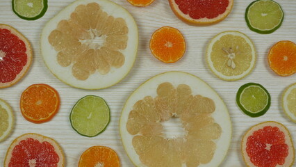 Slices of various citrus fruits on a light wooden background