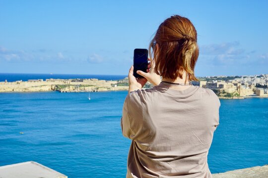 A female tourist taking a photo of the bay in Valletta, Malta, capturing the scenic coastal view