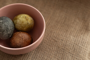 three easter eggs in a pink bowl on a burlap texture