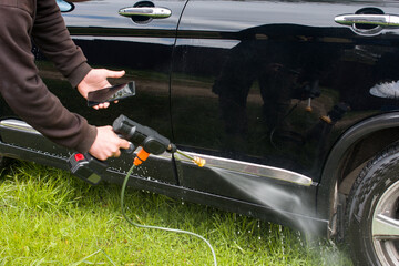 A man washes a car on the street. Washes dirt off the car with a water hose