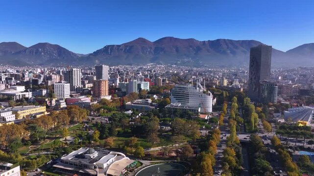 An aerial view of Tirana showcases the city's vibrant landscape, with Mount Dajt towering on the horizon. The mix of modern architecture, green spaces, and bustling streets creates a dynamic urban.
