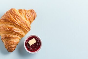 Golden croissant beside small bowl of red jam with butter pat on