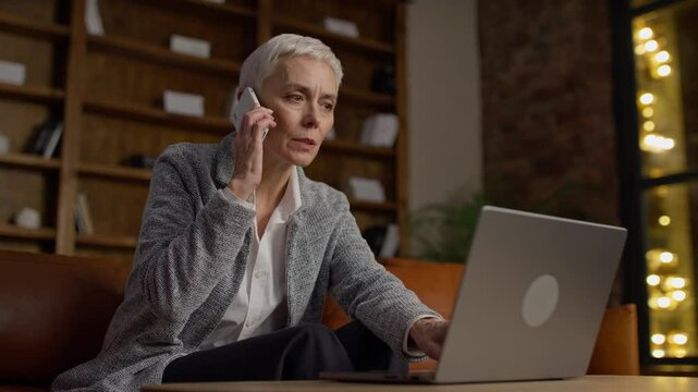 Frustrated senior businesswoman multitasking on phone and laptop