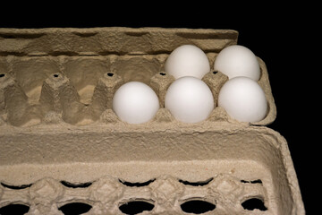 Five remaining unused white chicken eggs in an open carton box on a dark background