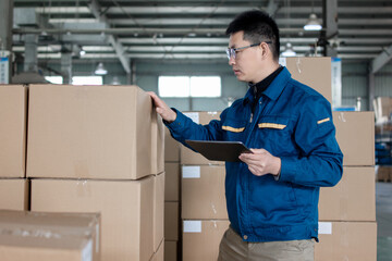 Middle-aged East Asian male blue-collar workers are using tablets in the factory warehouse. 