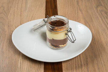 Dessert jar: layers of chocolate vanilla and cookie crumbs served on a white plate and wooden table