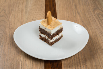 Delectable multi layered dessert with creamy filling a biscuit stick on white plate against wood...