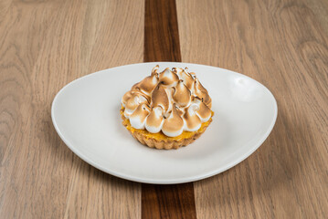 A lemon curd tart with toasted meringue peaks presented on a white plate and wooden table