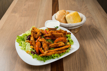 Delicious fried chicken salad with fresh vegetables and a side of rolls on a wooden table