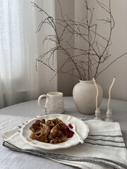 A beautifully arranged and styled table with a charming rustic design complete with delightful breakfast - crepes with jam, coffee, ceramic vase with elegant dry branches.