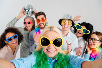 Group of colleagues celebrating in office with costumes and props against a grey background,...